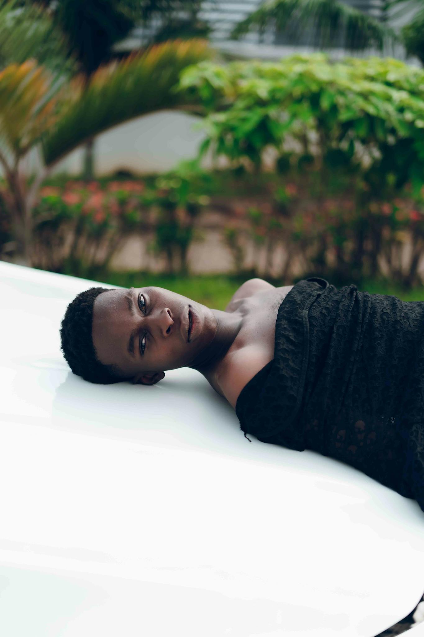 A captivating portrait of a person lying on a surface outdoors with lush greenery in the background.